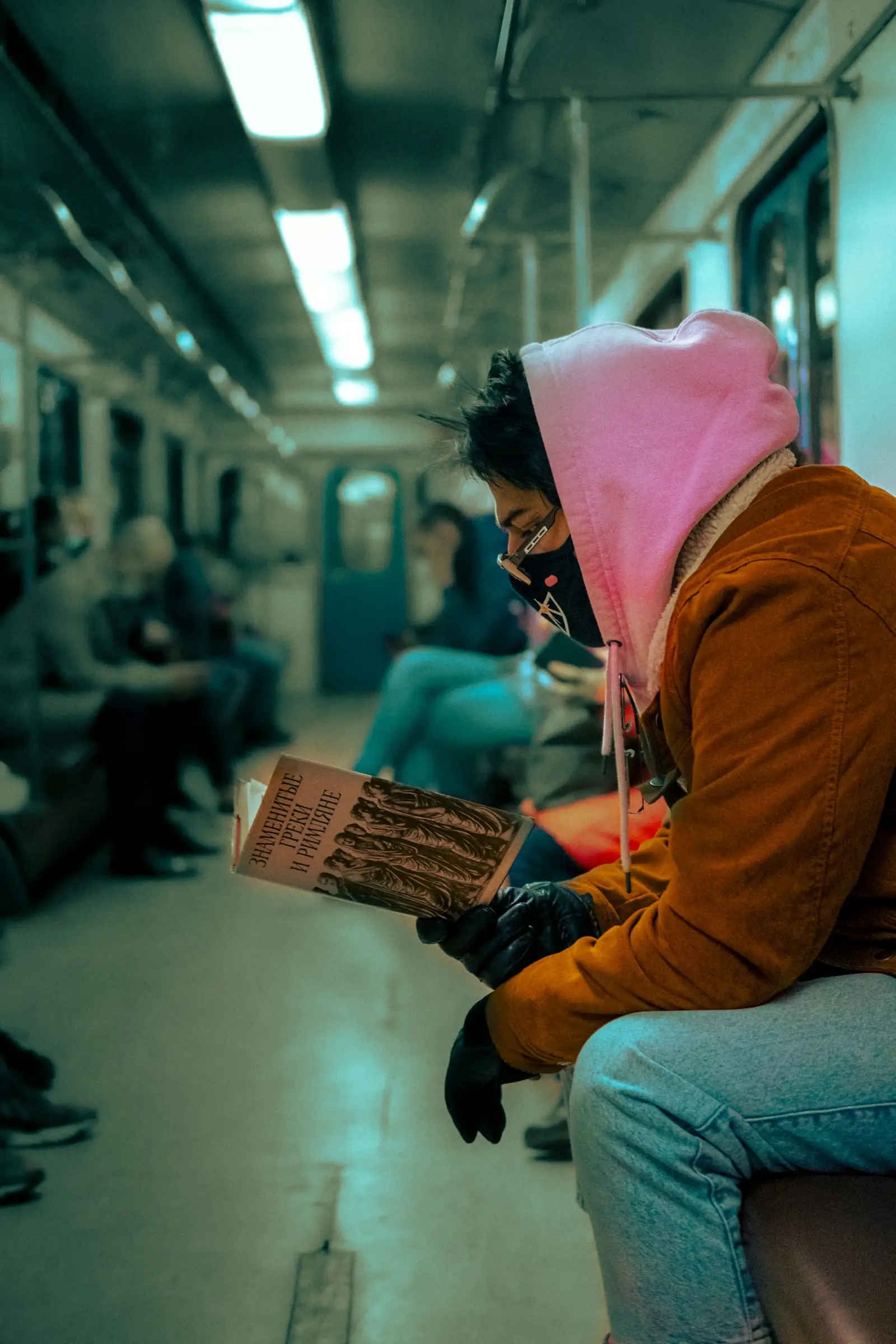 A commuter in a pink hood reads a magazine on a subway train